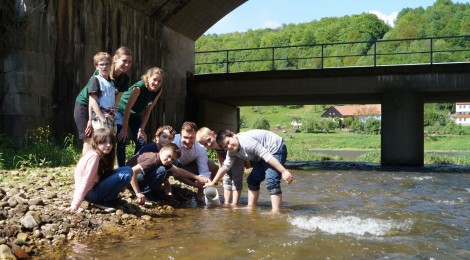 Der Königsteiner Bürgermeister Kummer schöpft mit Junior Rangern Taufwasser aus der Biela