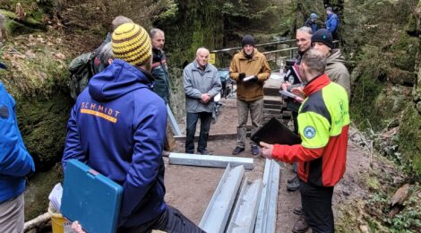 Foto: Hp. Mayr Bei der gestrigen öffentlichen Bauberatung stellte Uwe Borrmeister (3. v. r.) Leiter der Nationalpark- und Forstverwaltung Sächsische Schweiz vom Sachsenforst die Baumaßnahmen an den Steiganlagen in den Schwedenlöchern den berührten Bürgermeistern und der Presse vor. Bauingenieur Martin Aulitzky (r.) von der Nationalpark- und Forstverwaltung erläuterte die nächsten Schritte des Baus mit dem neuen von Hand heran transportierten Stahlträgern. Harry Dintner (Mitte links) aus Lohmen, hat 1967 am Bau der bisherigen Stufenanlagen mitgewirkt und interessierte sich sehr für die Rekonstruktion der Stiegen.