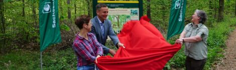 Foto: A. Kurby Lehrerin Chris Dittrich von der Grundschule Berggießhübel, Bürgermeister Thomas Peters und Revierleiterin Annett Wehner enthüllen schwungvoll die neue Tafel, die am Eingang des neuen Waldlehrpfades an der Rasthütte Bethlehemstift steht.